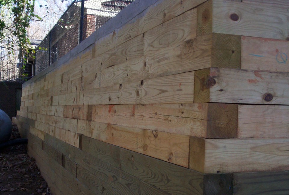 Pressure Treated Timber Retaining Wall w/ 'Deadman' Anchors built as Base for Poured Three Lane Driveway / Parking Area w/ Black Chain Link Fence