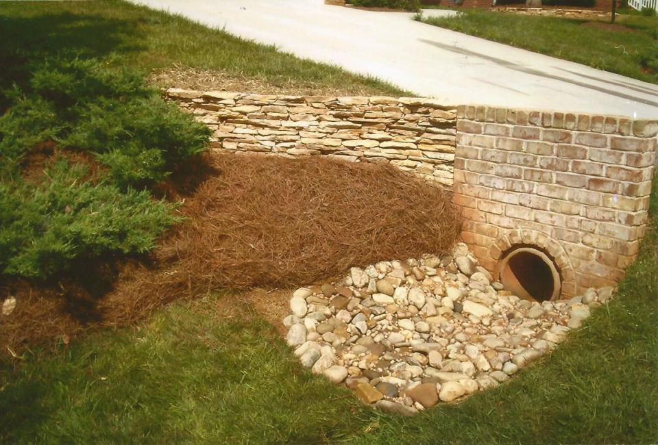 Tan Brick Housing Surrounding Driveway Drainage Piping Accentuated w/ ArkansasThin Veneer Retaining Wall & River Slicks at Base of Drainage Area Dry Creek Bed